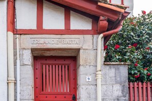 Entrada de un edificio con puerta roja, una placa de piedra con la inscripción 'ERLANDE-BATA' y el número '9'.