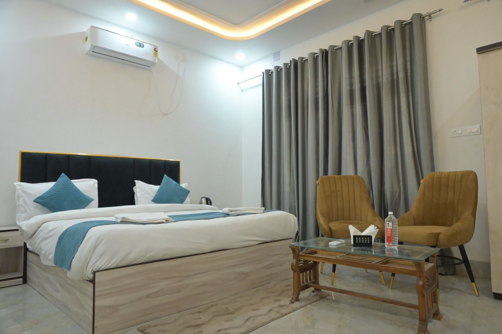 Una habitación de hotel moderna con cama, dos sillones, una mesita de centro de cristal y un amplio ventanal con cortinas.
