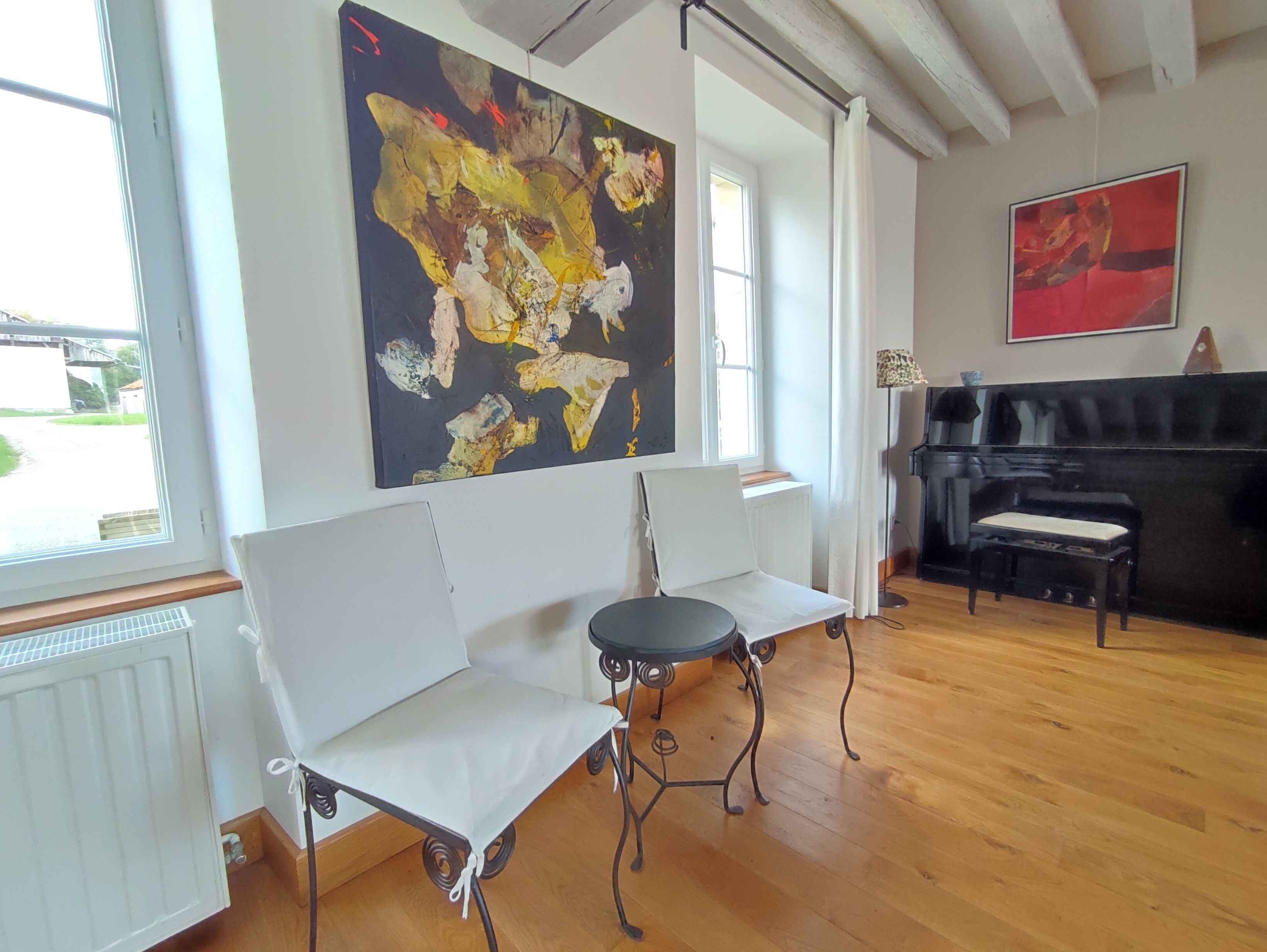 A room with a white sofa, a small round table, and a large abstract painting on the wall.