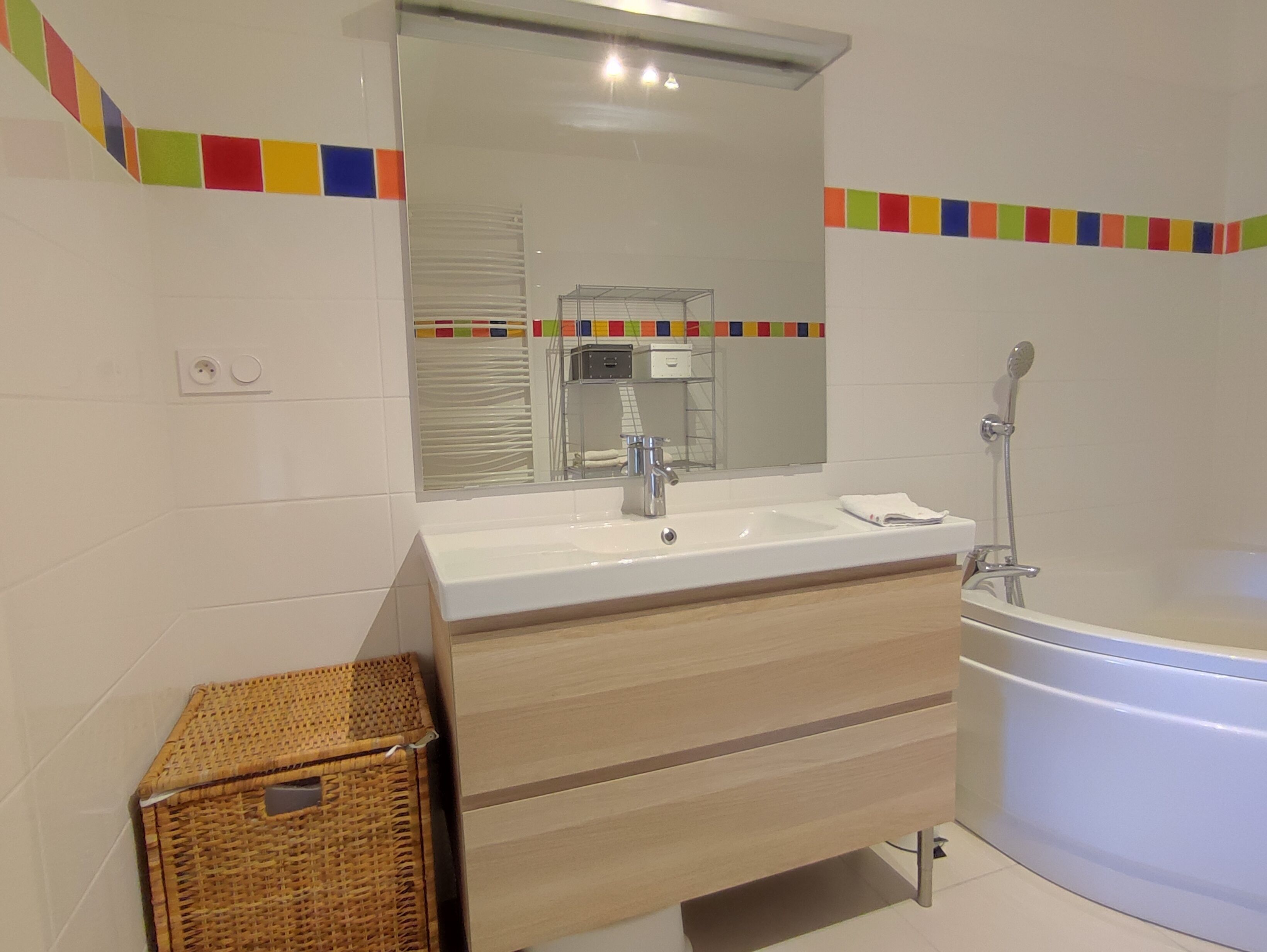 Une salle de bain moderne avec un lavabo blanc, un meuble-lavabo en bois, un grand miroir et une baignoire.