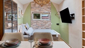 Ein Zimmer mit Backsteinwand, einem Bett, einem an der Wand befestigten Fernseher und einem Esstisch mit Tellern und einem Weinglas.