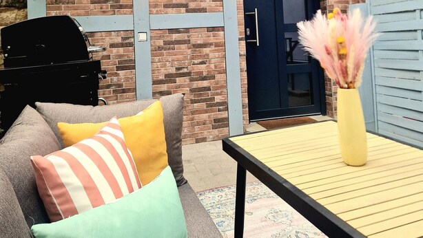 Ein Patio mit Ziegelmauer, einer Tür, einem Grill und einem Tisch mit einer Vase.