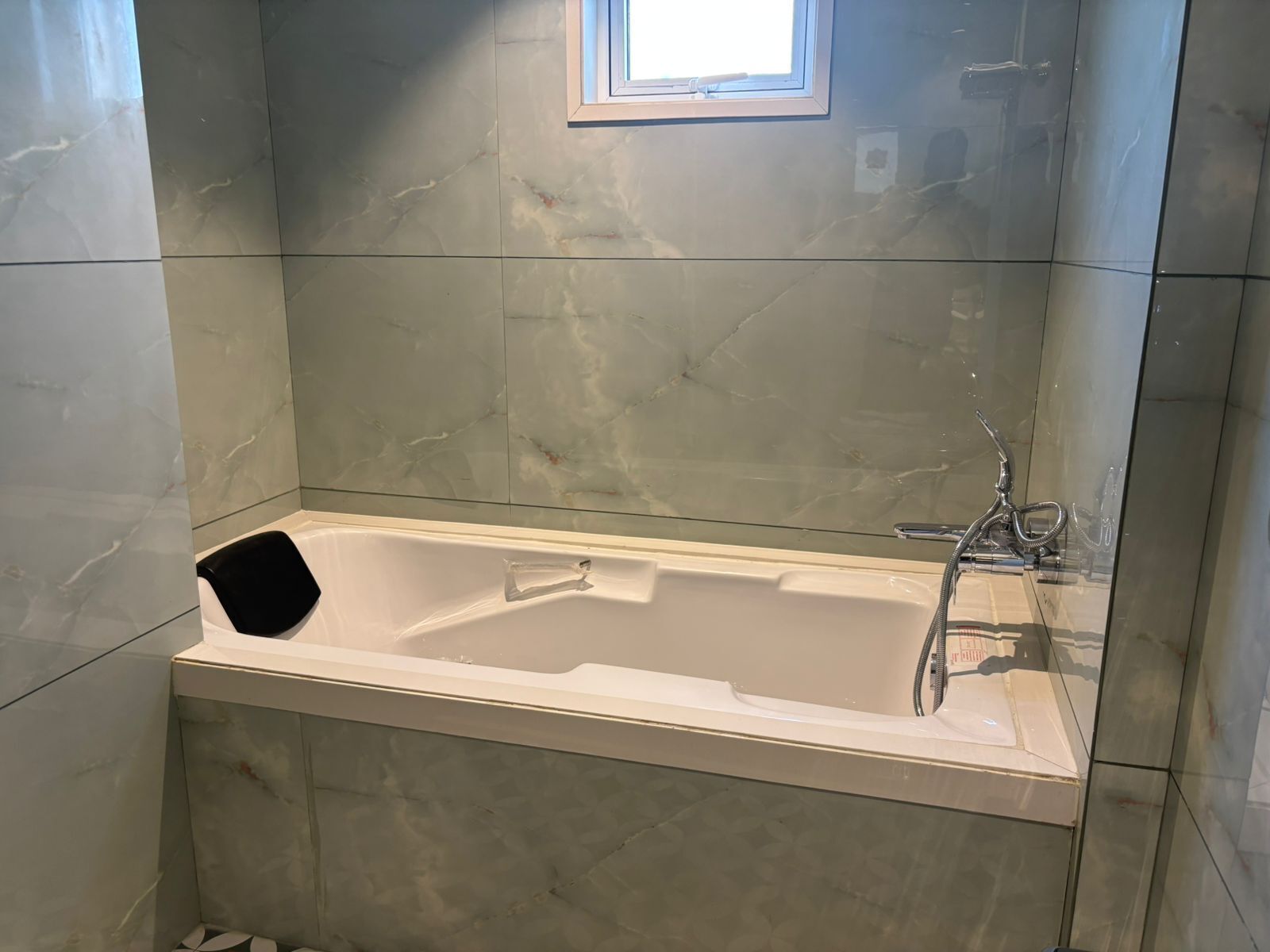 A bathroom with a white bathtub, a glass shower enclosure, and a small window above the tub.