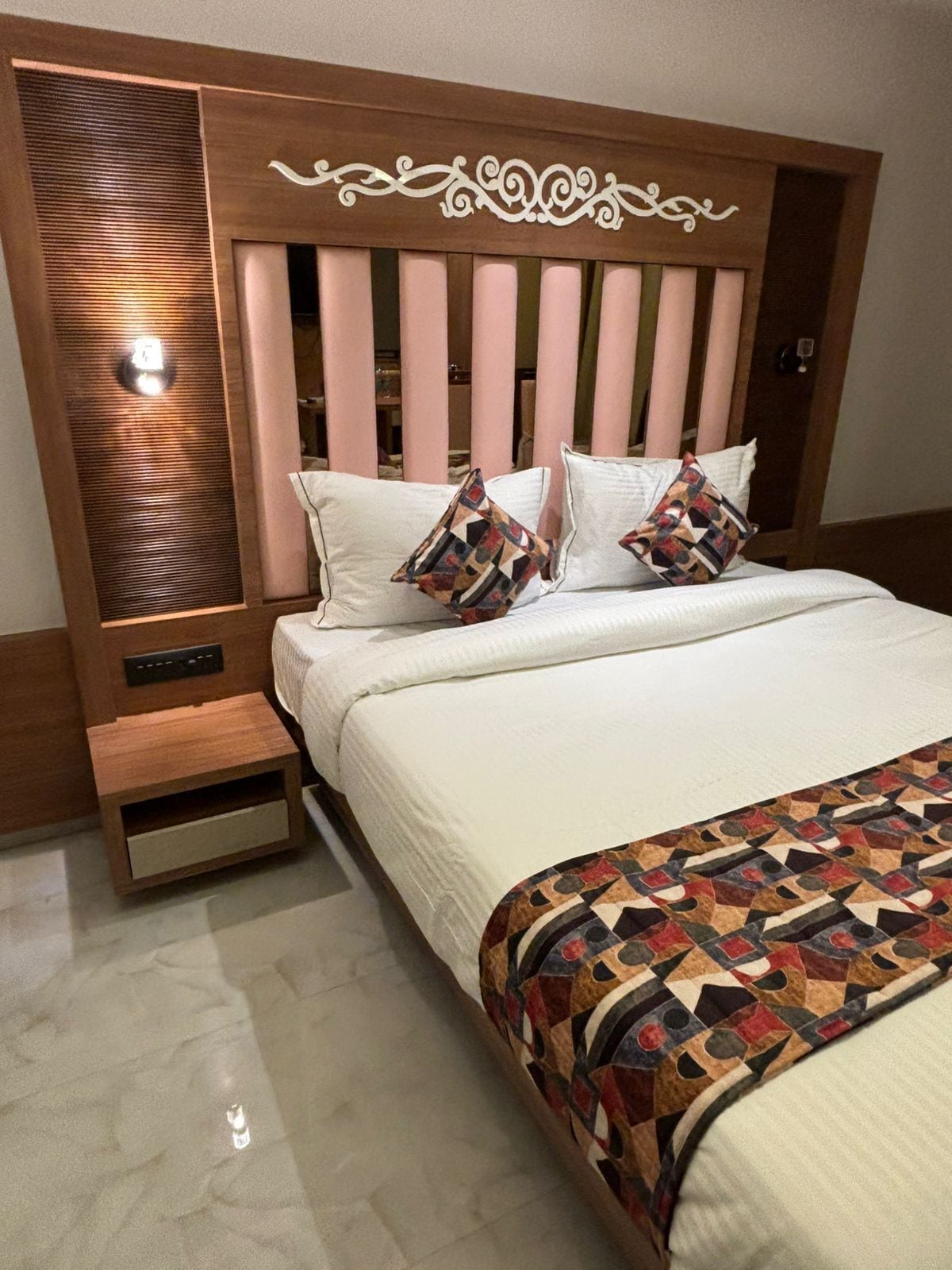 Un dormitorio ordenado con cabecera de madera, una mesita de noche y una colcha estampada.