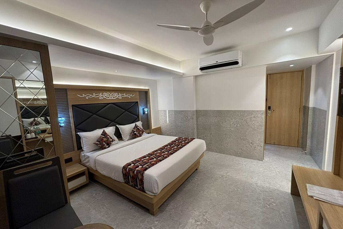 Een moderne hotelkamer met een groot bed, een plafondventilator, een airconditioningapparaat, een houten deur en een klein bureau met een stoel.