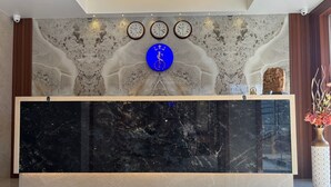 Een receptiebalie met een marmeren blad, drie wandklokken en een blauw rond bord.