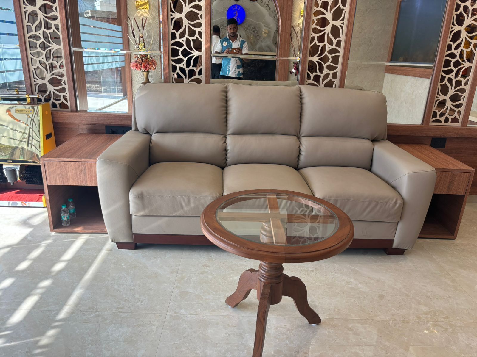 A beige sofa with a glass-top coffee table in a modern room with patterned wooden panels.