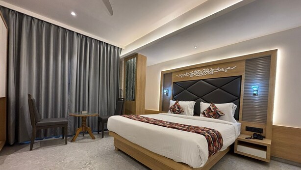 Een moderne hotelkamer met een groot bed, een kleine tafel, een stoel en een groot raam met gordijnen.