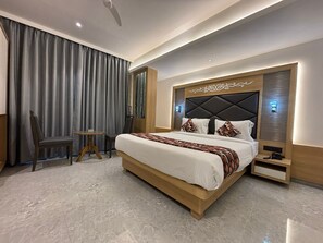 A modern hotel room with a large bed, a small table, a chair, and a large window with curtains. - Hotel Imperial Suites - Airoli (Navi Mumbai)