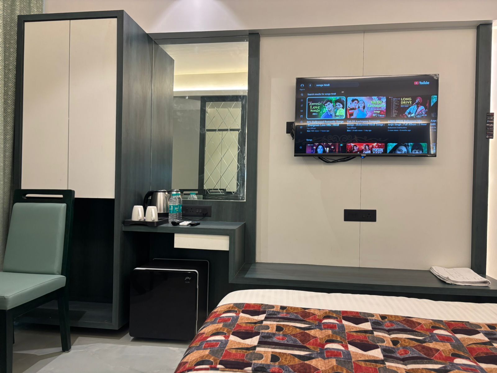Habitación de hotel con cama, escritorio con computadora, silla, televisor montado en la pared y ventana.