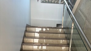 Een trap met afwisselend beige en donkerbruine treden, een glazen leuning en een metalen handrail.
