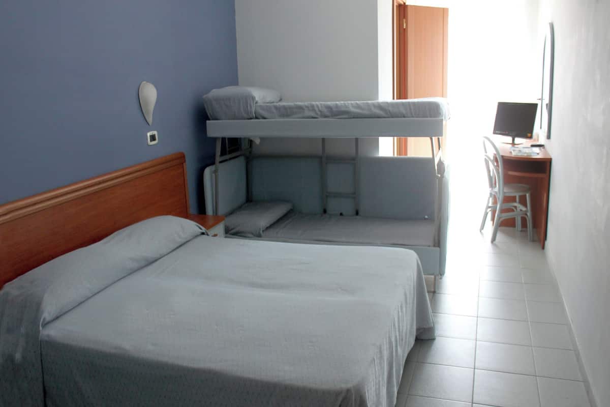 A room with two beds, a desk with a chair, and a window.