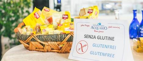 A table with a gluten-free sign, a wicker basket of snacks, and a coffee machine in the background.