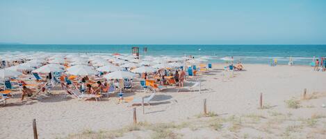 Une plage dotée de nombreuses chaises longues et de parasols, d’une tour de surveillance pour les sauveteurs, et d’une étendue de sable.