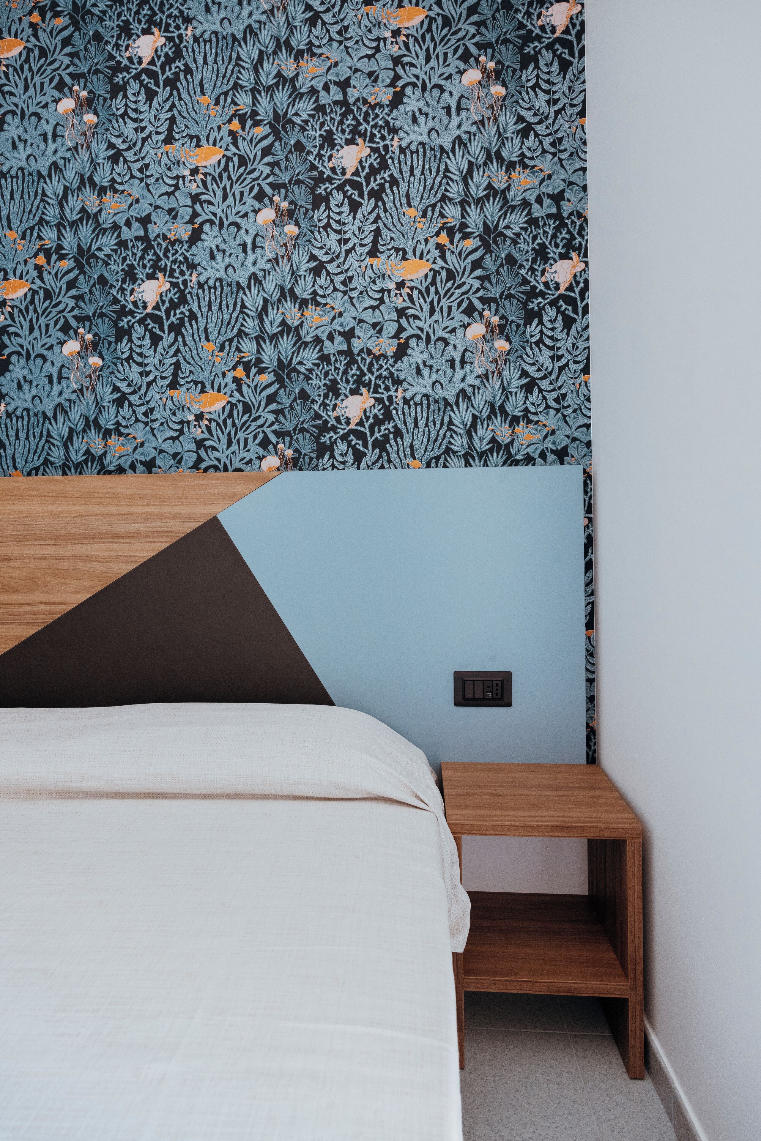 A bedroom with a bed, a nightstand, and a wall with a leaf-patterned wallpaper.