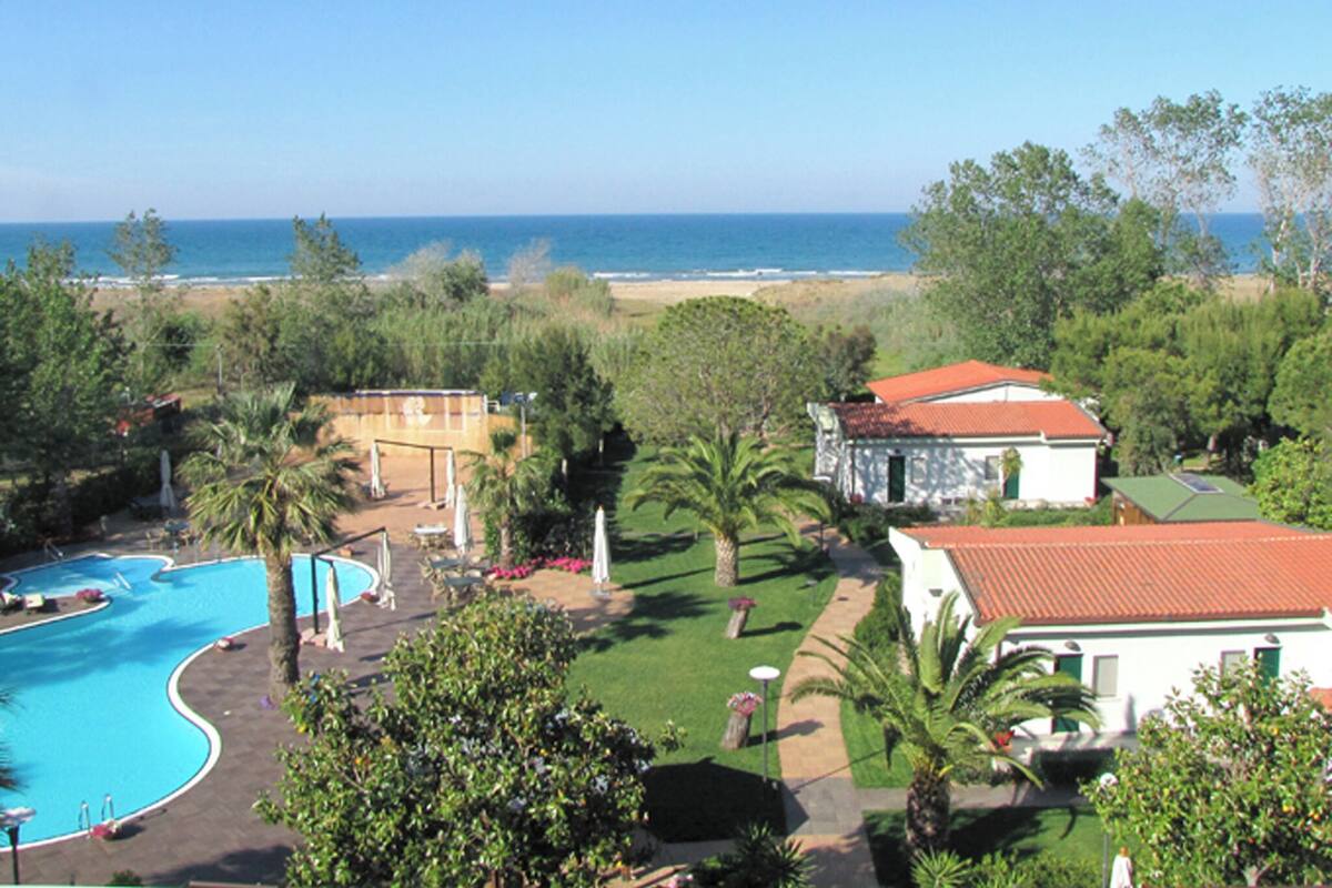 A resort with a swimming pool, a beach view, and a building with a red roof.