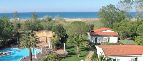 Ett semesterhotell med en swimmingpool, utsikt över stranden och en byggnad med ett rött tak.