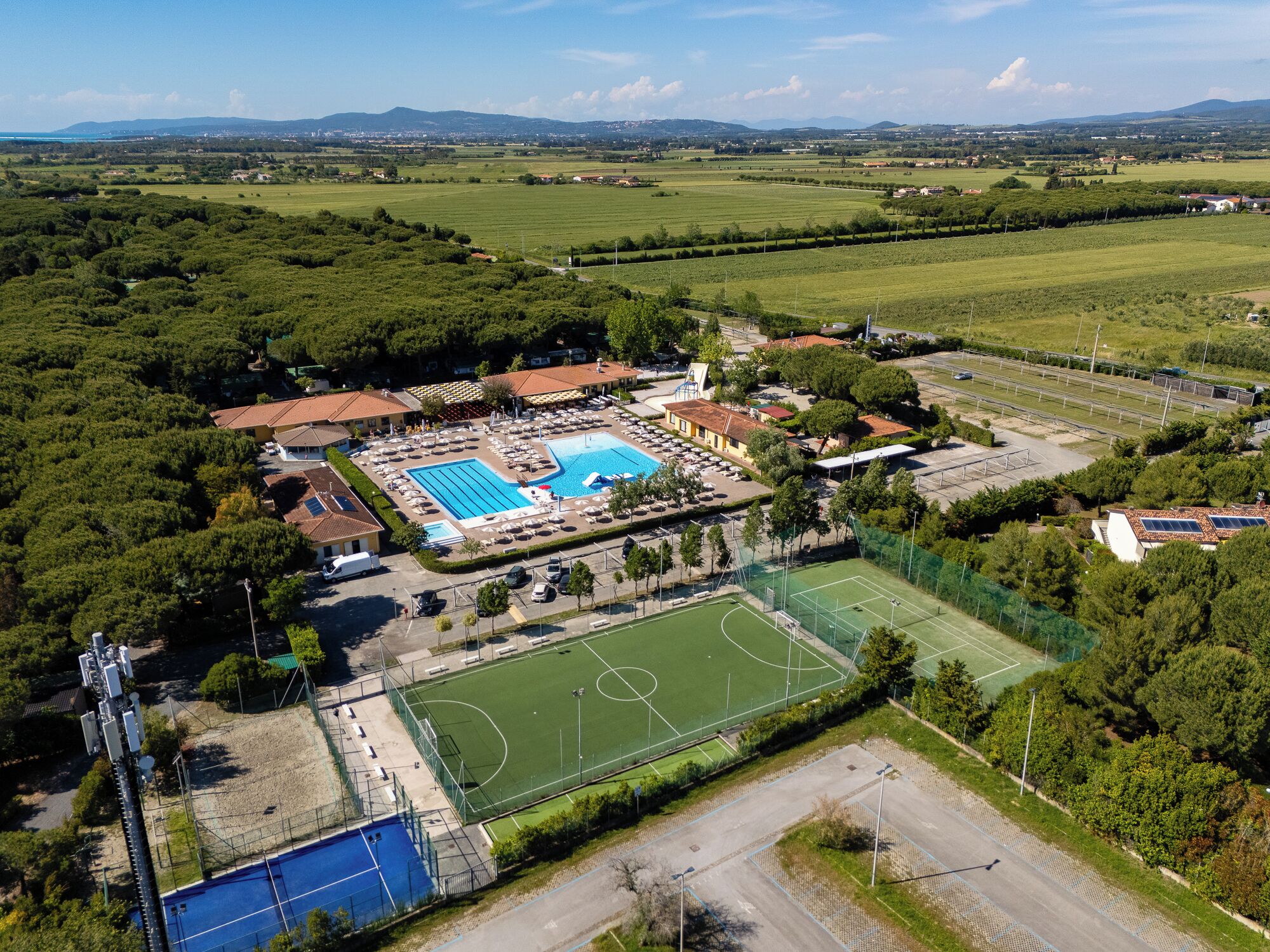 Eine Luftaufnahme eines Sportkomplexes mit Schwimmbad, Tennisplätzen und einem Fußballfeld.