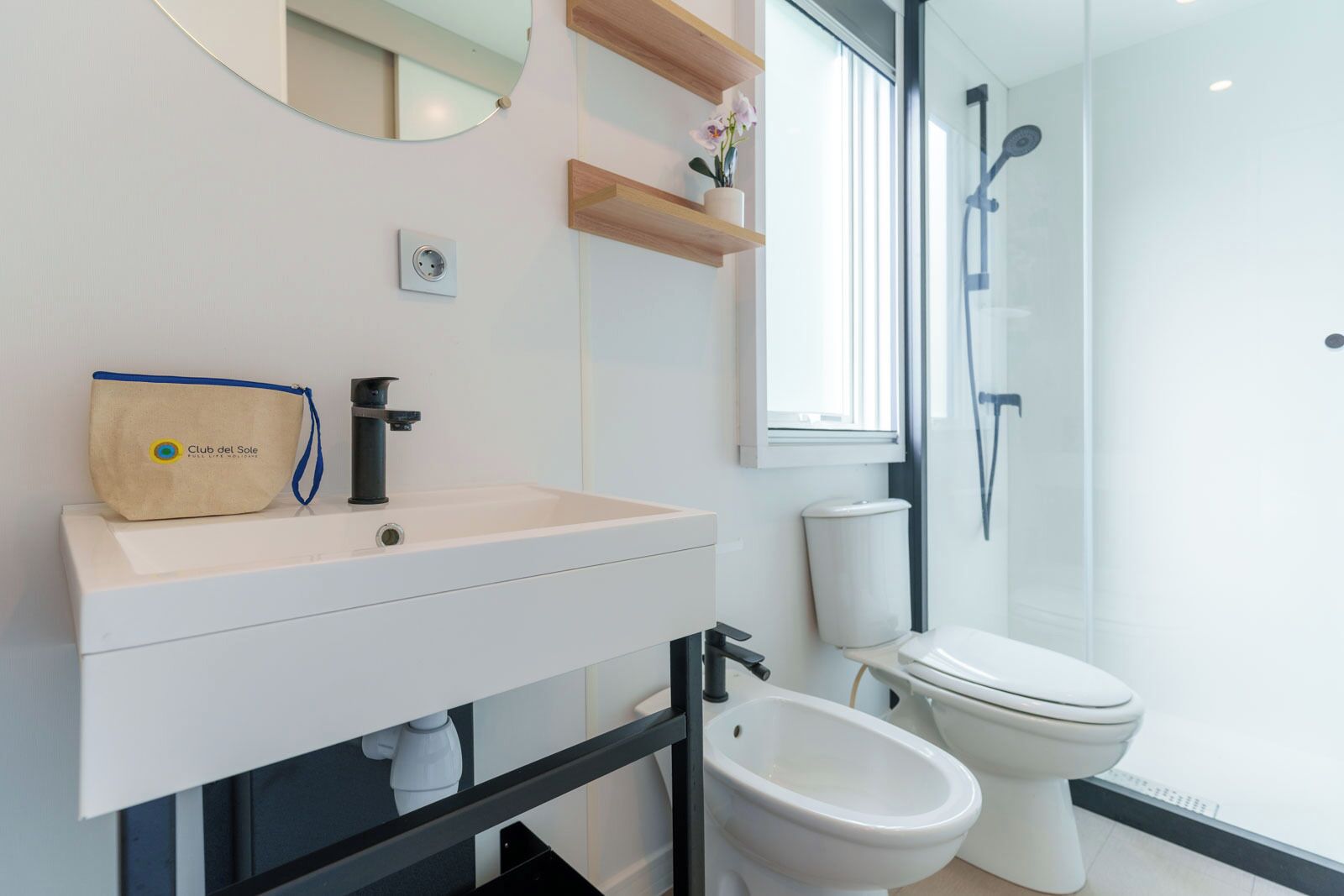 Et moderne badeværelse med hvid vask, bidet, toilet, bruser og spejl.