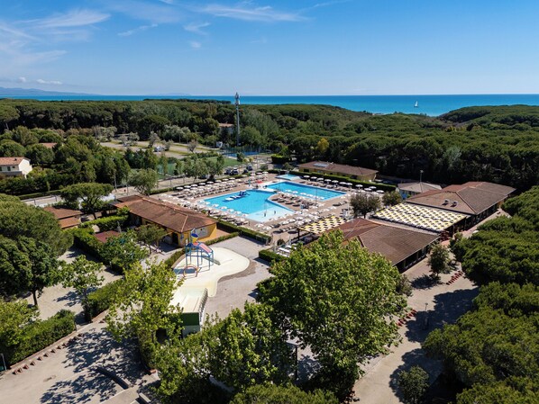 Eine Luftaufnahme eines Resorts mit einem zentral gelegenen Schwimmbad, Liegestühlen und Blick aufs Meer.