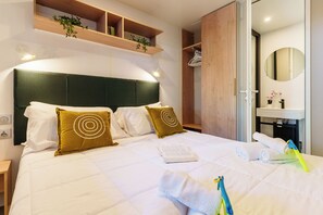 Ein Hotelzimmer mit einem großen Bett, einem Holz-Kopfteil, einem eingebauten Kleiderschrank, einem Nachttisch und einem Badezimmer mit Spiegel und Waschbecken.