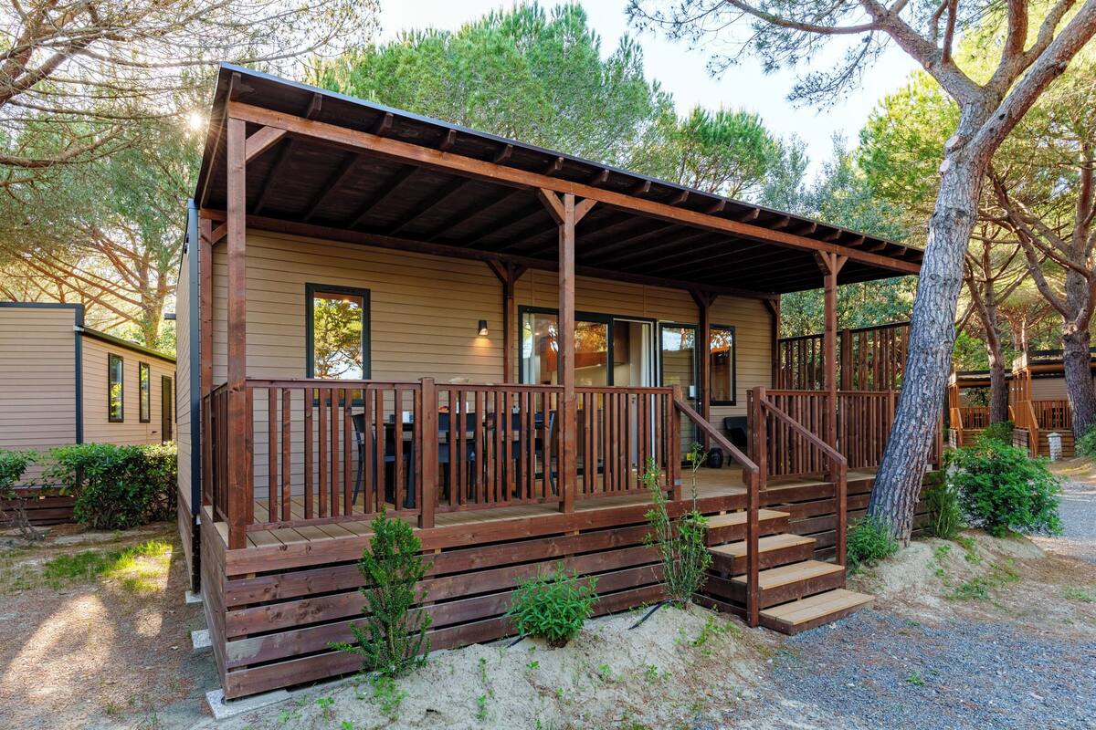 Una cabaña de madera con un porche, una escalera y vistas a árboles circundantes.