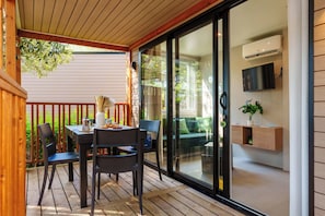 A modern outdoor dining area with a table, chairs, and a view of the garden through glass doors.