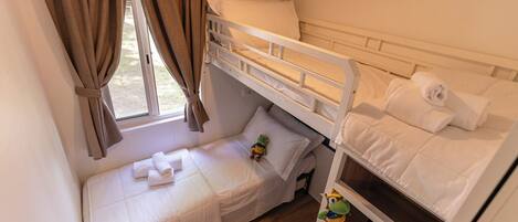Una habitación pequeña y funcional con una cama nido, una cama individual y un ventanal con cortinas.