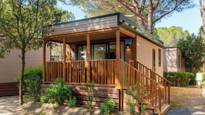 A single-story wooden cabin with a porch, a visible door, and a mailbox. - Club del Sole Le Gorette Cecina Easy Camping Village (Cecina)