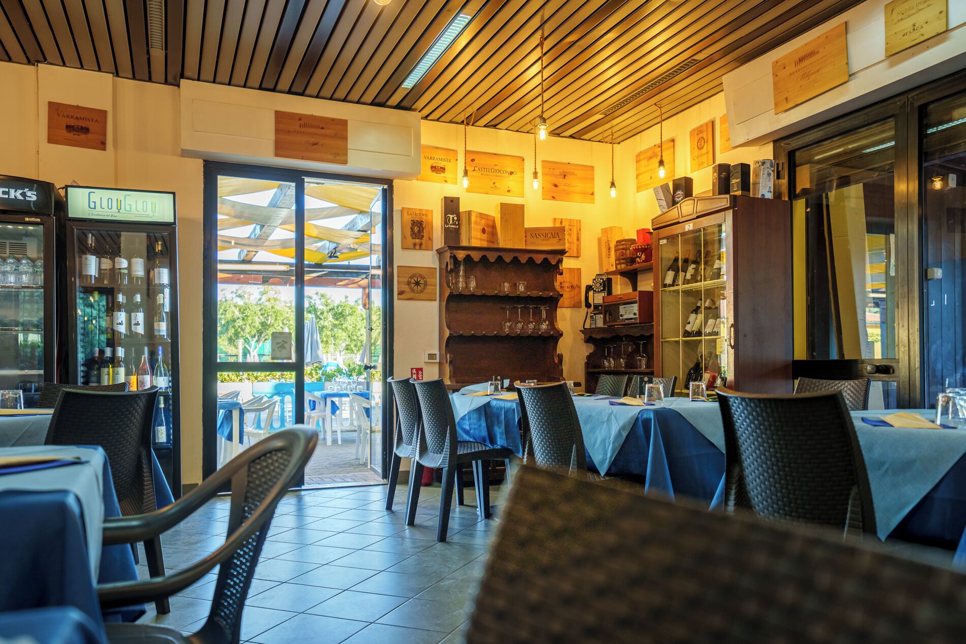 Un restaurante con mesas y sillas, una exhibición de vinos y vistas al exterior.