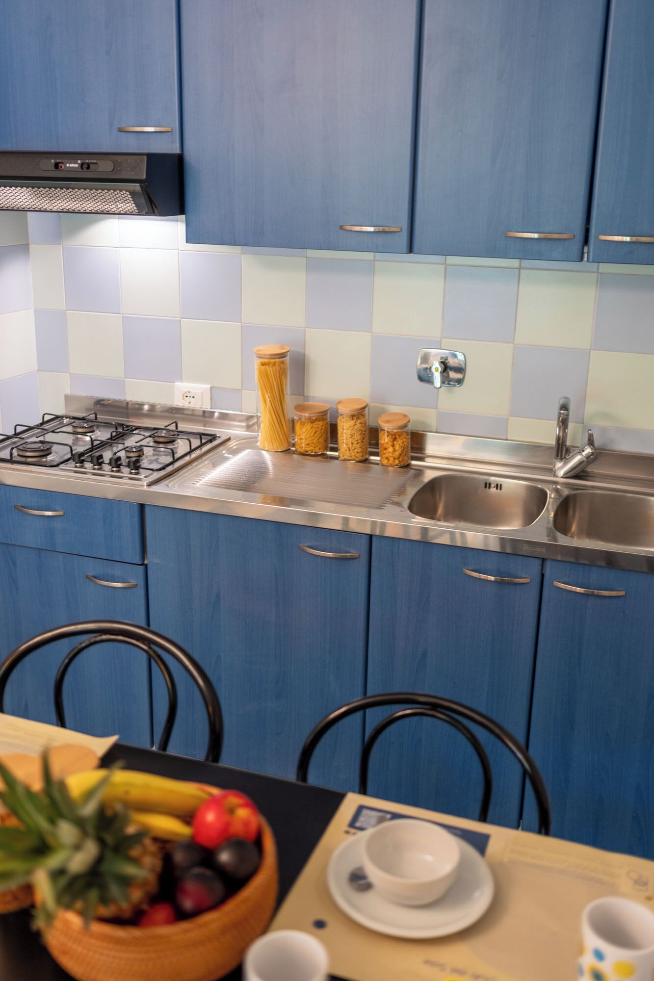 A kitchen with blue cabinets, a gas stove, stainless steel sink, and a tiled backsplash.