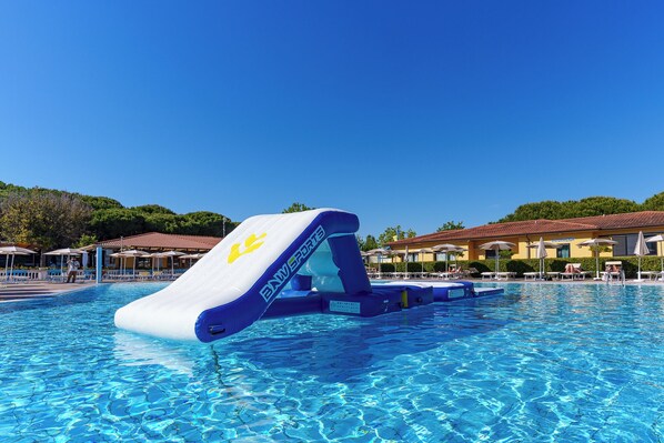 A swimming pool with a water slide, lounge chairs, umbrellas, and a building with a tiled roof in the background.