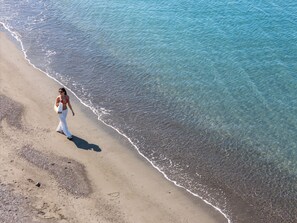 A beach scene with clear water and a person walking along the shore.