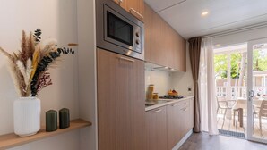 A modern kitchen with wooden cabinets, a built-in microwave, and a dining area with a table and chairs. - Club del Sole Le Gorette Cecina Easy Camping Village (Cecina)