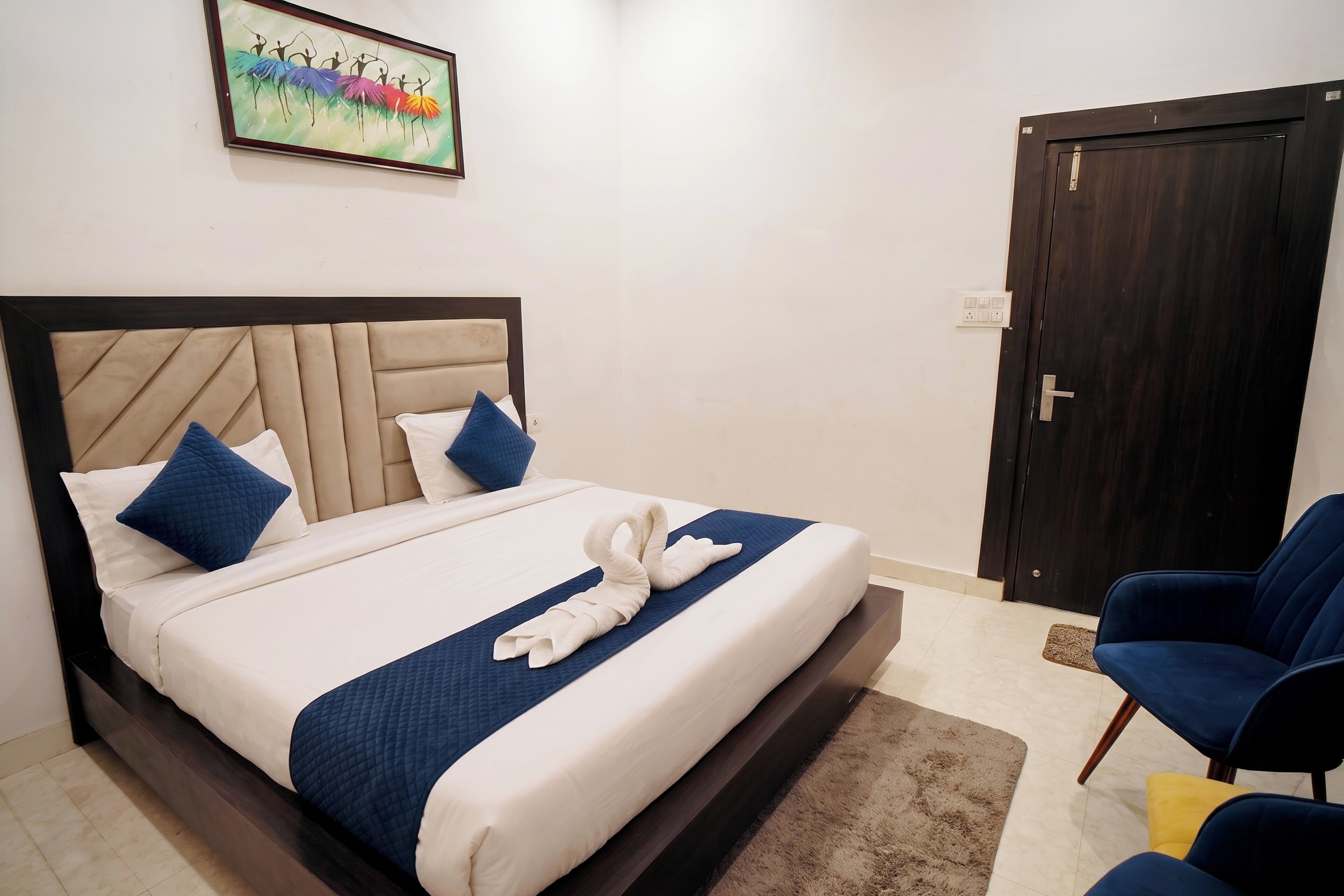 A hotel room with a bed, a chair, a door, and a painting on the wall.