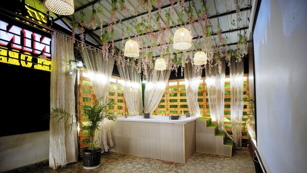 A room with a reception desk, a potted plant, and a staircase with a green wall. - The Nines Hotel & Restro (Haldwani)