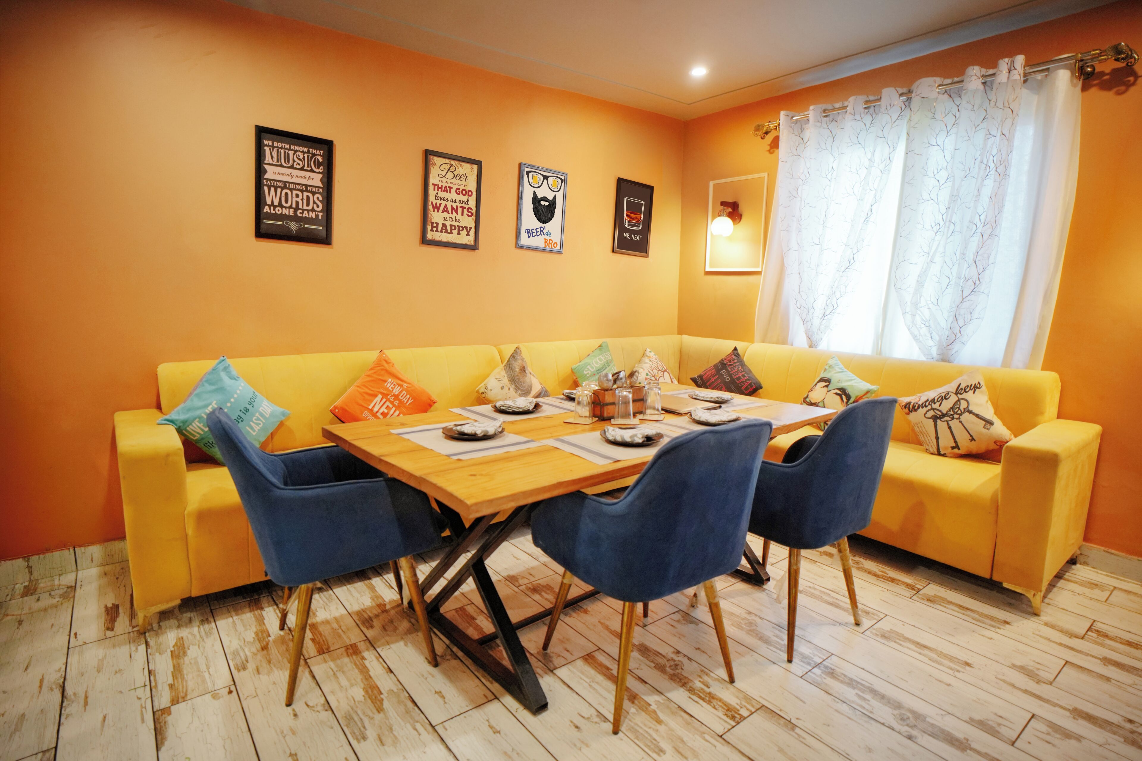 Un comedor con un sofá amarillo, sillas azules, una mesa de madera y un ventanal con cortinas.