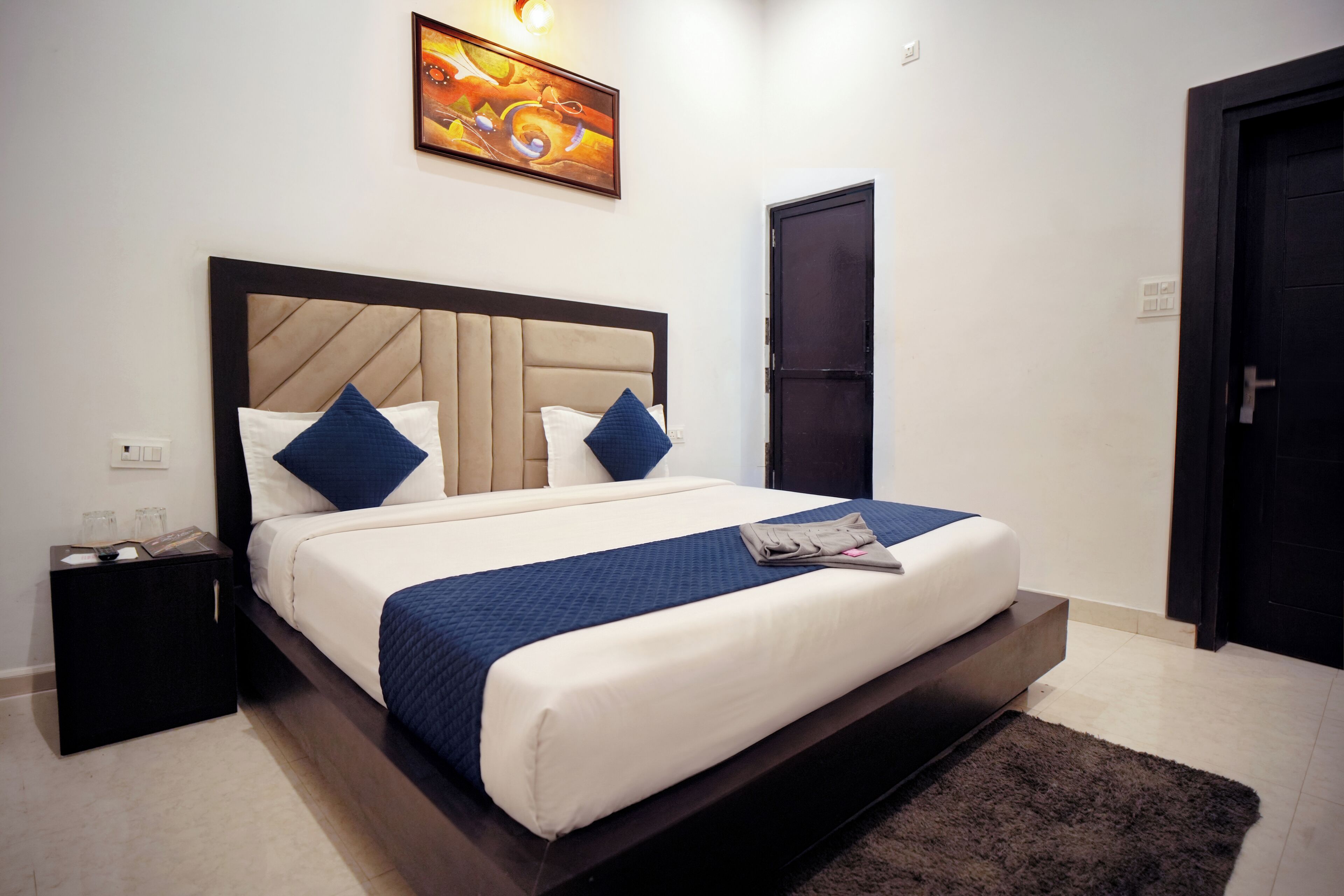 Habitación de hotel con una cama grande, una mesita de noche, una puerta y una obra de arte colgada en la pared.