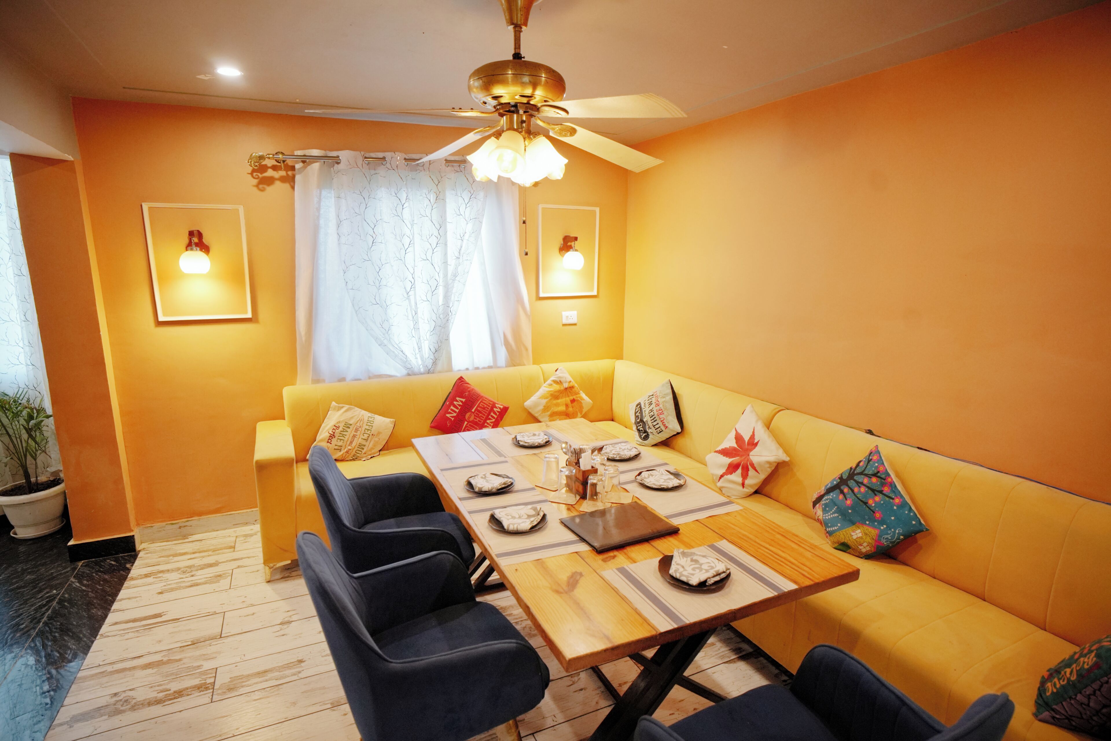 Un comedor con un sofá amarillo, una mesa de madera dispuesta para dos personas y un ventilador de techo.