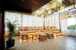 A cozy seating area with a sofa and wooden tables, surrounded by curtains and hanging lights. - The Nines Hotel & Restro (Haldwani)