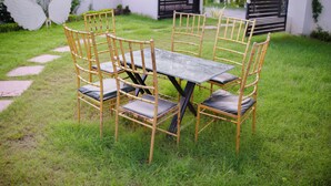 A rectangular outdoor table with four chairs, surrounded by a grassy area with a pathway leading to a gate. - The Nines Hotel & Restro (Haldwani)