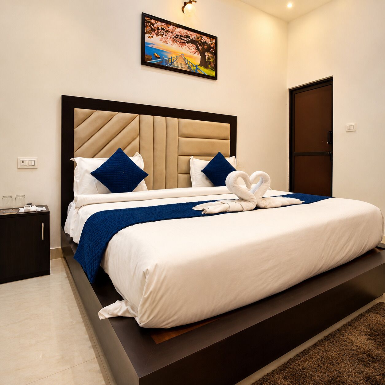 A hotel room with a large bed, a headboard, a nightstand, and a painting on the wall.