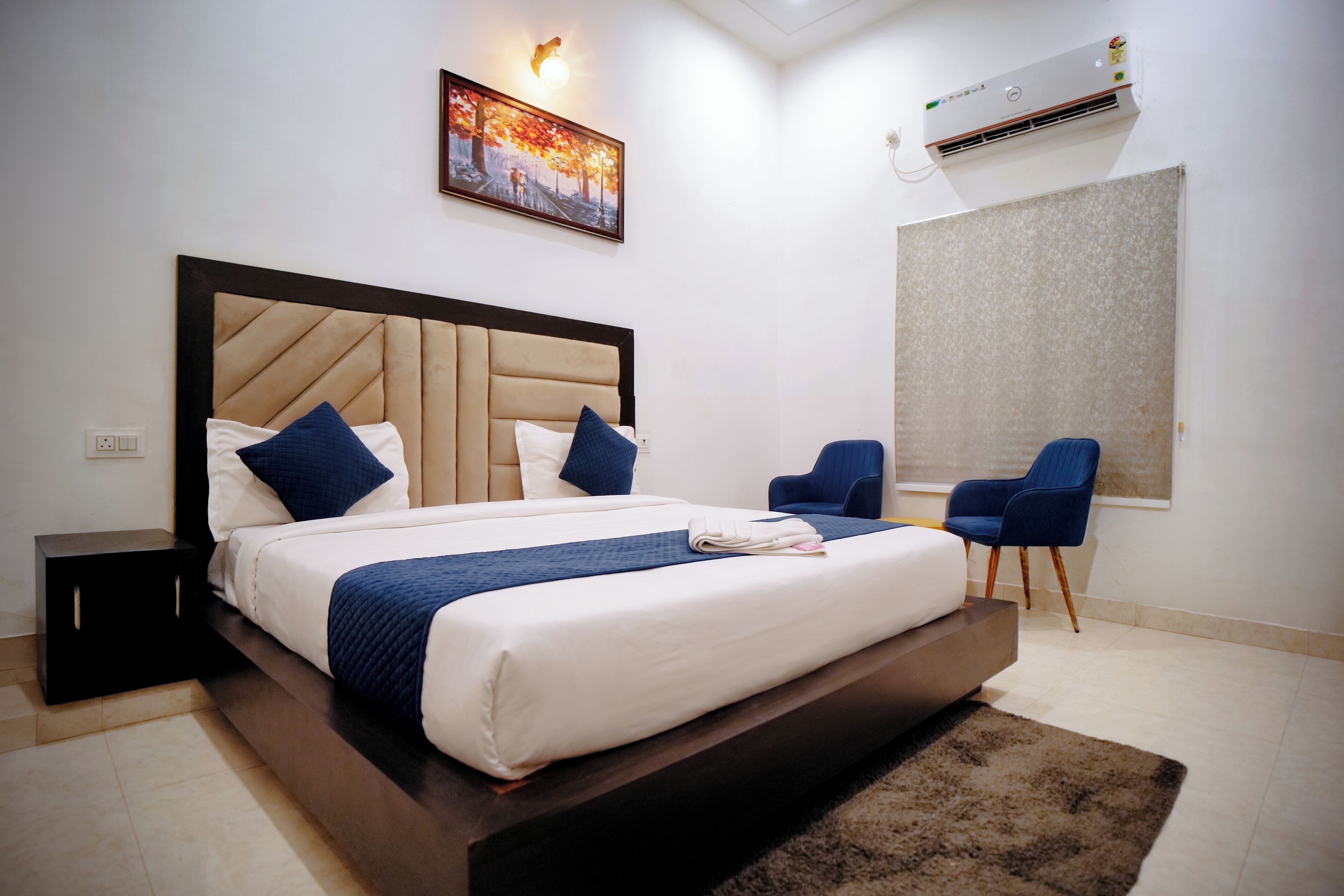 Une chambre d’hôtel moderne équipée d’un grand lit, d’une tête de lit, d’une table de chevet, d’une chaise, d’une fenêtre et d’un appareil de climatisation.