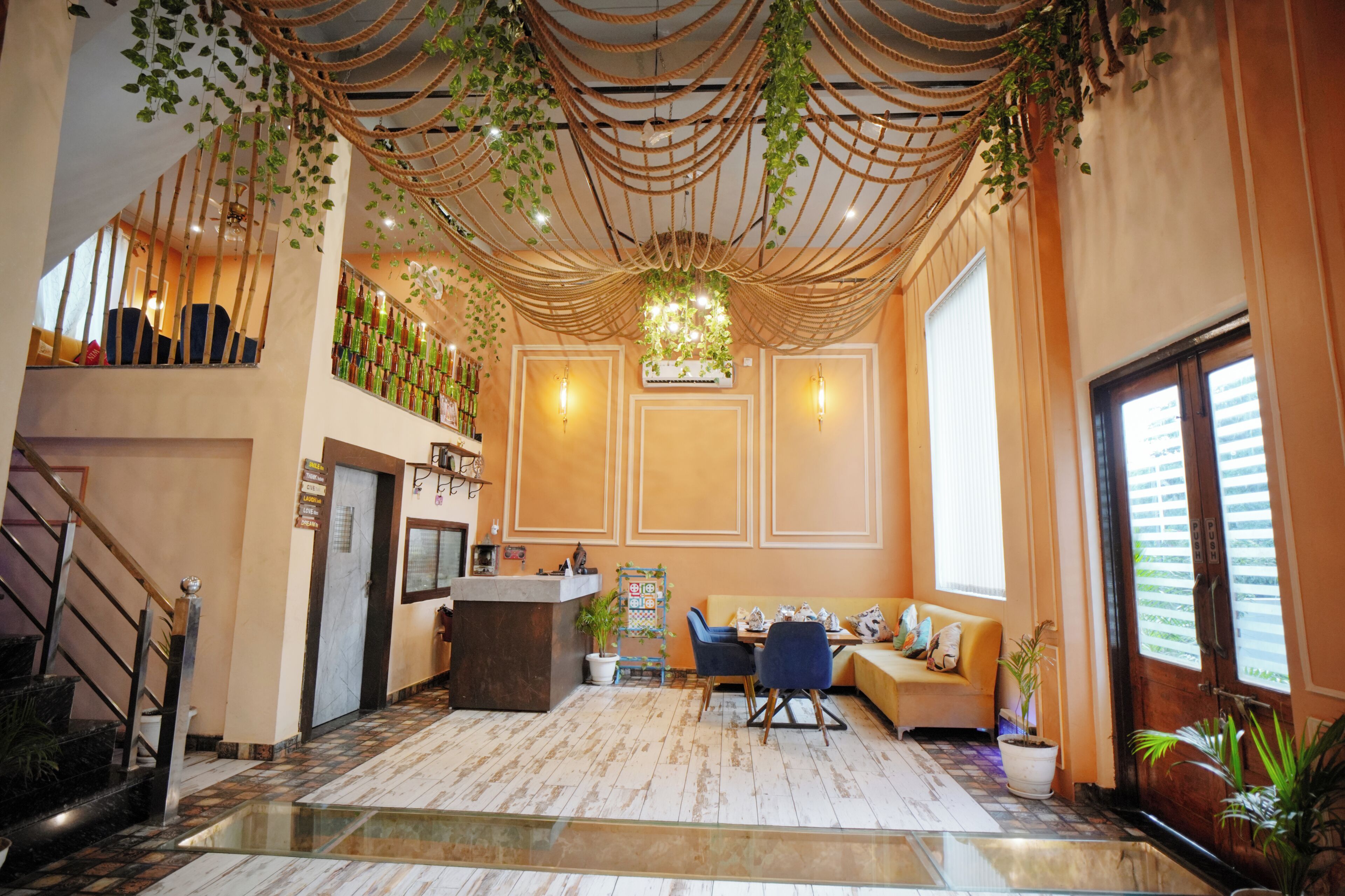 A hotel lobby with a reception desk, seating area, staircase, and decorative plants.