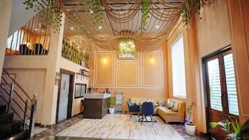 A hotel lobby with a reception desk, seating area, staircase, and decorative plants.