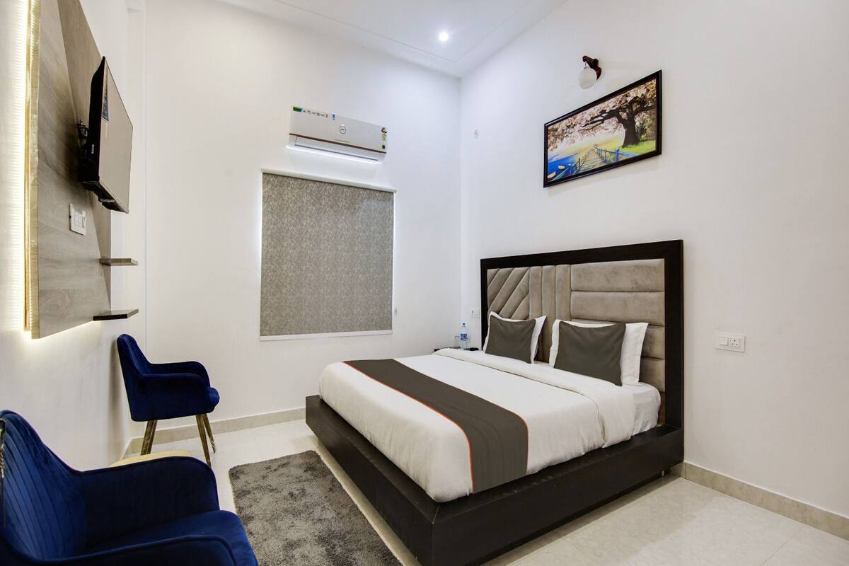 Un dormitorio moderno con cama, televisor montado en la pared, ventana con persianas y un cuadro de un puente.