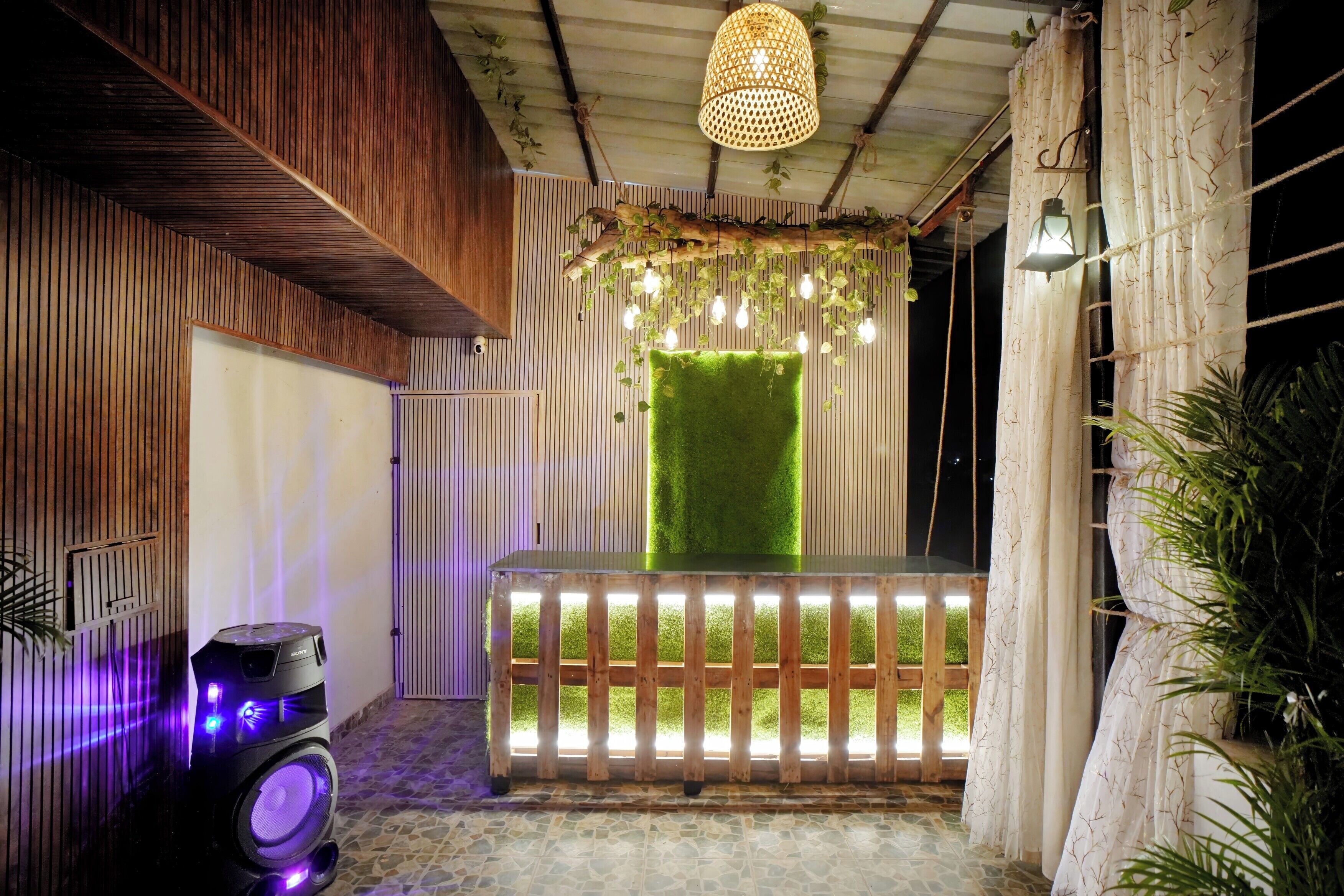 Una habitación con pared de listones de madera, pared de césped artificial verde, un banco de madera y un altavoz con luces moradas.