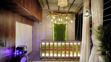 Una habitación con pared de listones de madera, pared de césped artificial verde, un banco de madera y un altavoz con luces moradas.