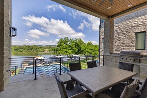 A covered patio with a table and chairs, a grill, and a view of a lake with boats.