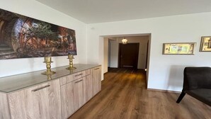 Un pasillo con piso de madera, un aparador de vidrio con candelabros de latón y un sofá negro.